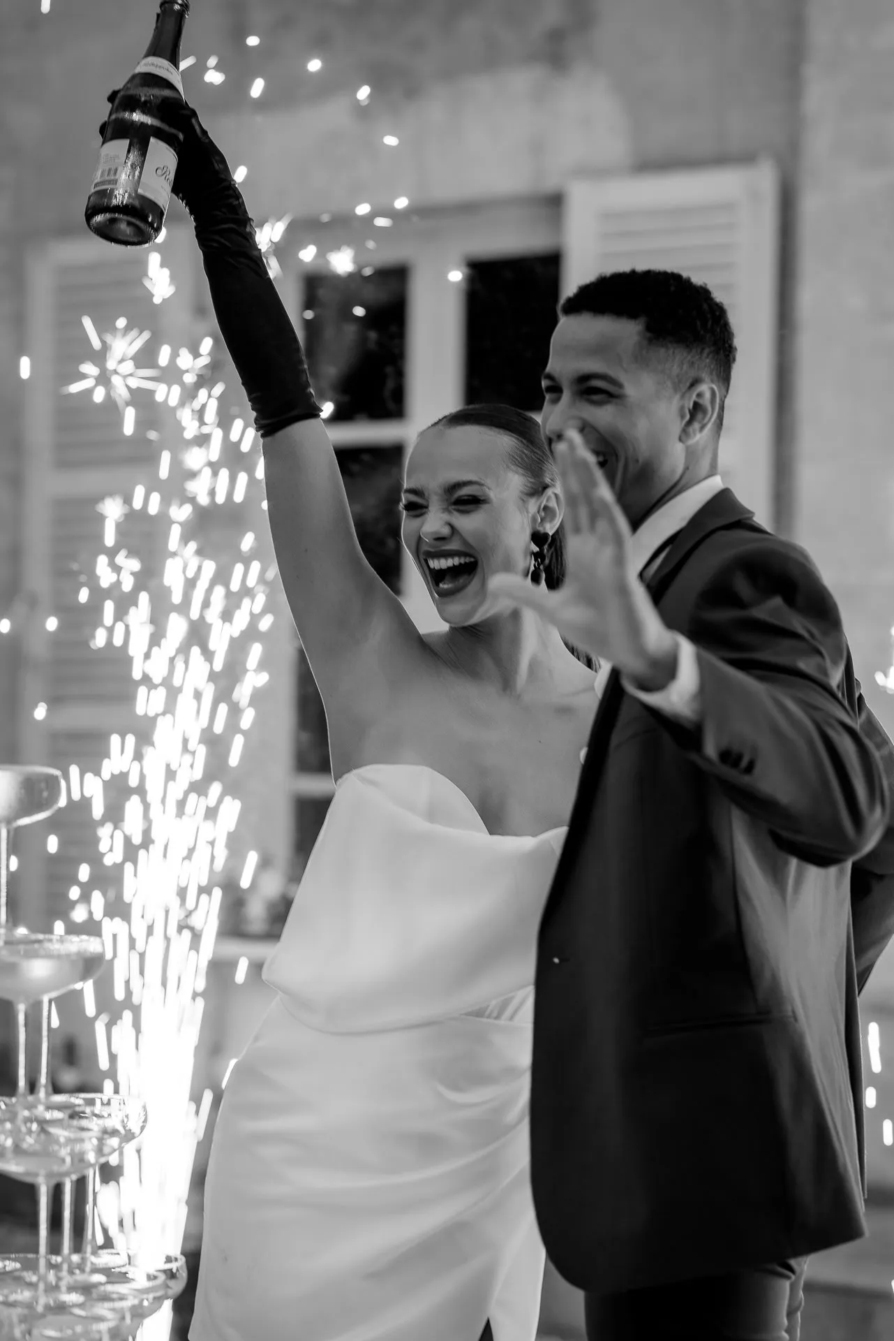 Jubilant bridal couple celebrating with champagne bottle and fireworks in black and white at Chateau de Varennes